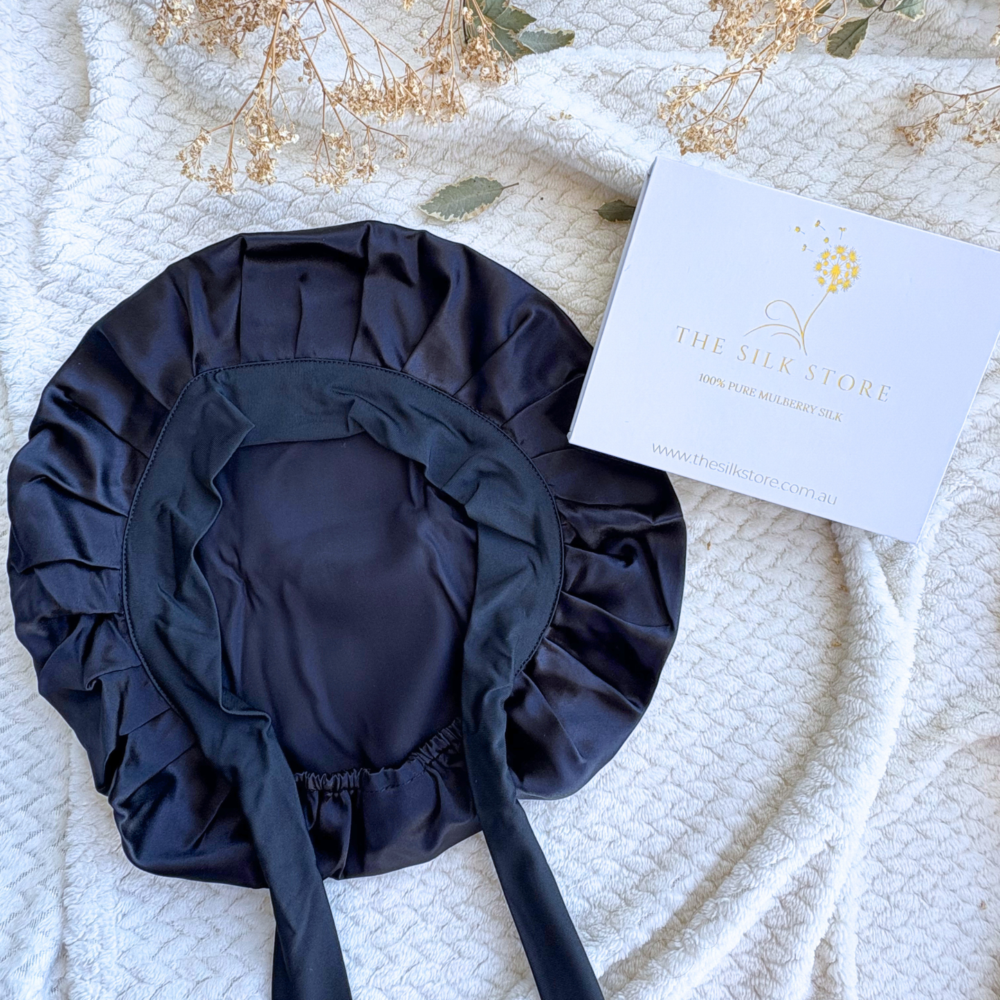 black silk bonnet on a textured white surface with a branded box.